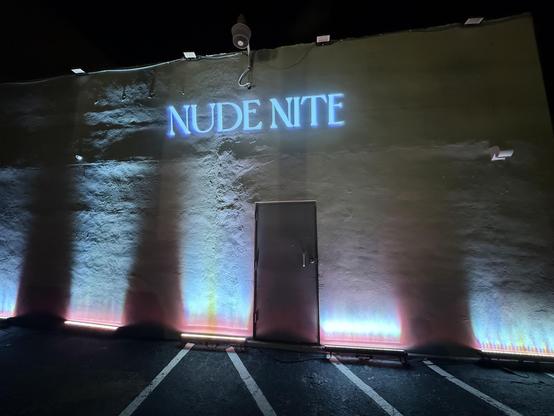 The side of a white building with “Nude Nite” projected on the side.  